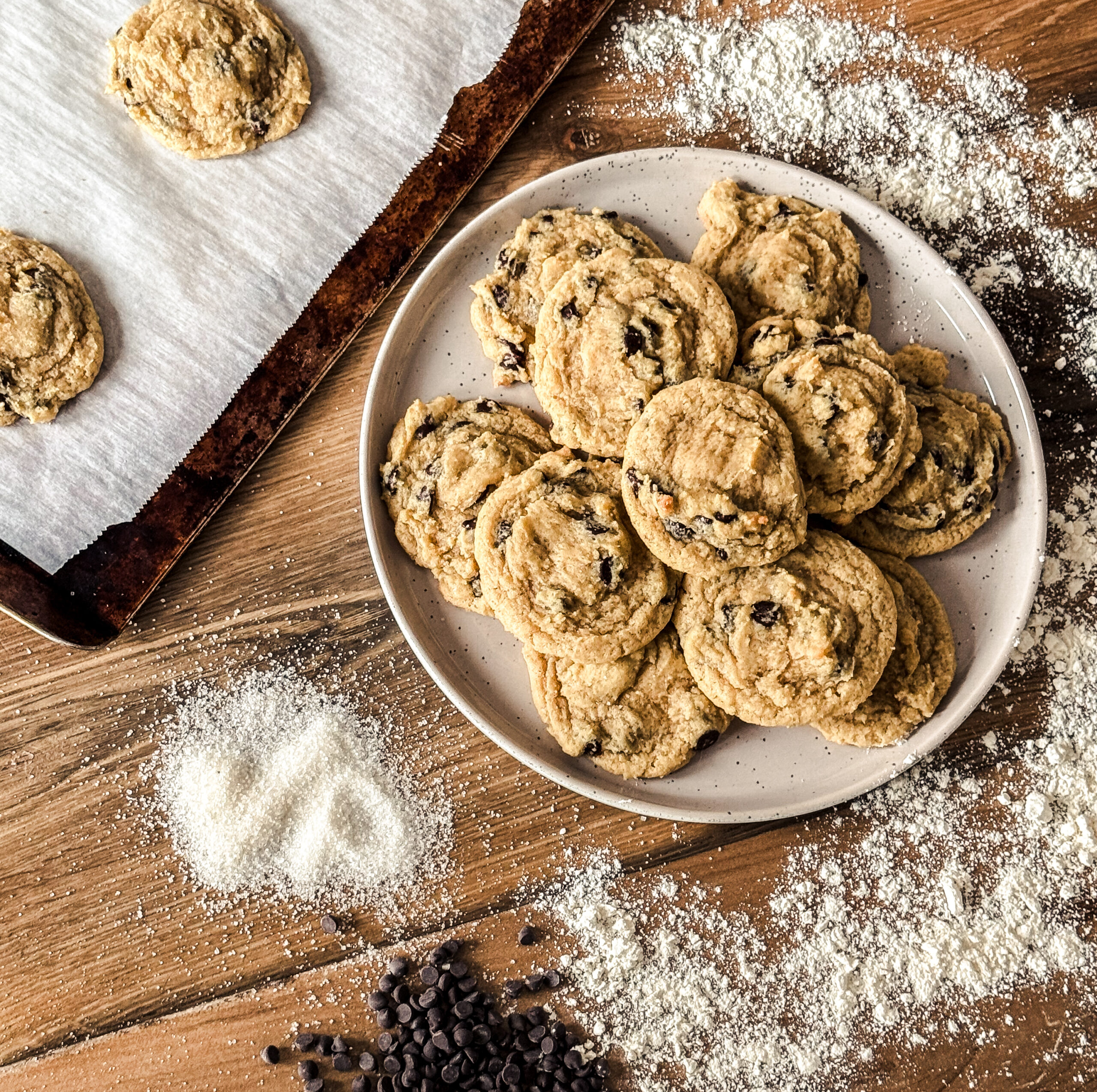 Gooey Einkorn Chocolate Chip Cookies with melted chips on a plate surrounded by flour and sugar.