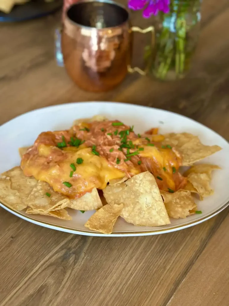 Slow cooker chicken enchilada nachos piled high on a platter, topped with melted cheese.