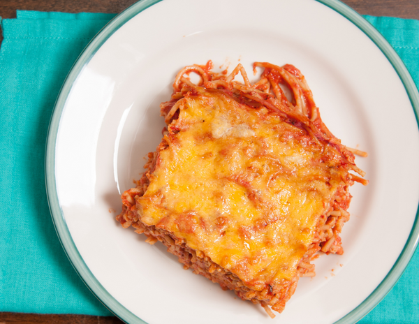 A golden, cheesy casserole dish filled with layers of spaghetti, meat sauce, and melted cheese, garnished with fresh herbs.