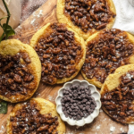 Pecan Pie Cookies sitting on a cutting board near a small container of chocolate chips in the sun