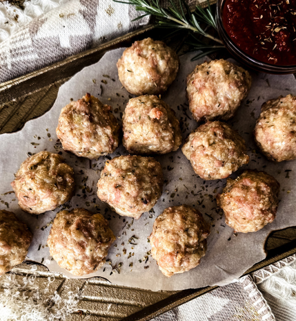 White textured background, gold tray with parchment paper, 12 meatballs on top.