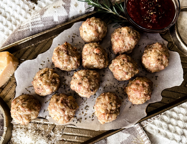 White textured background, gold tray with parchment paper, 12 meatballs on top.