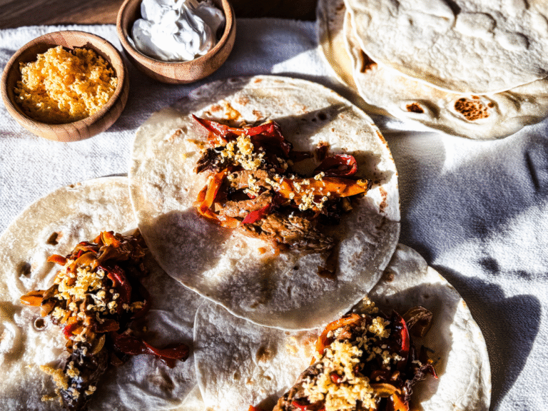 3 steak tacos laid out flat with 2 small bowls filled with cheese and sour cream.