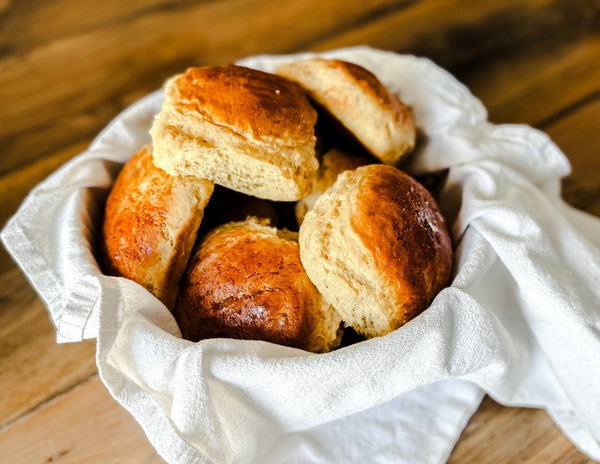 A batch of golden, fluffy Hawaiian buns with a shiny, buttery glaze, arranged in a basket, ready to be served for dinner or sandwiches.