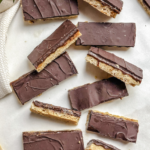 homemade candy bars sliced into thin bars layered with cookie, caramel, and chocolate and laying all around a small white tea towel