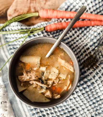 A comforting bowl of hearty chicken noodle soup with tender shredded chicken, egg noodles, carrots, celery, and fresh parsley, served hot with a spoon.
