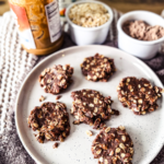 Neutral textured background with a gray plate. On the plate is 6 chocolate no-bake high protein cookies.