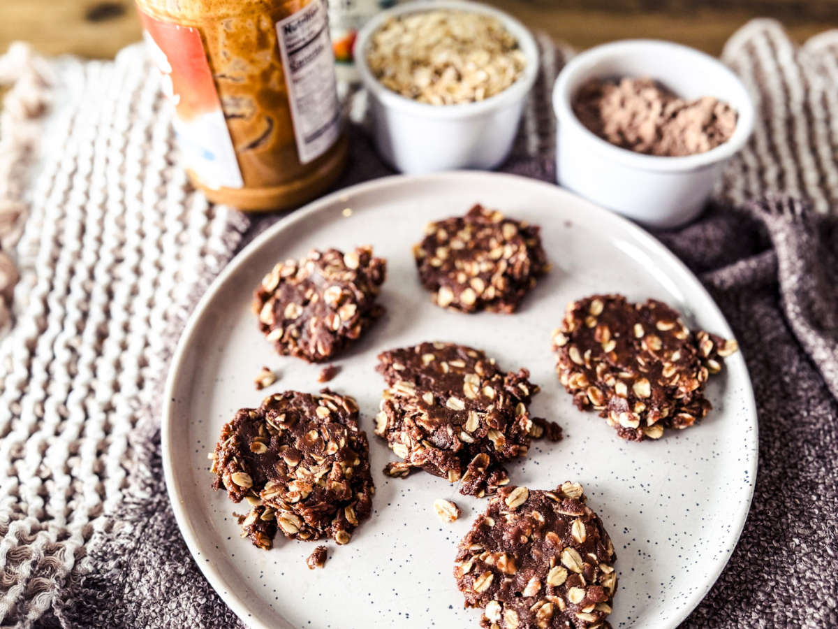Neutral textured background with a gray plate. On the plate is 6 chocolate no-bake high protein cookies.