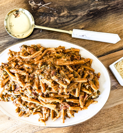 A delicious plate of pasta coated in creamy tomato sauce, topped with crispy bacon pieces. Served on a white plate on a rustic wooden table.