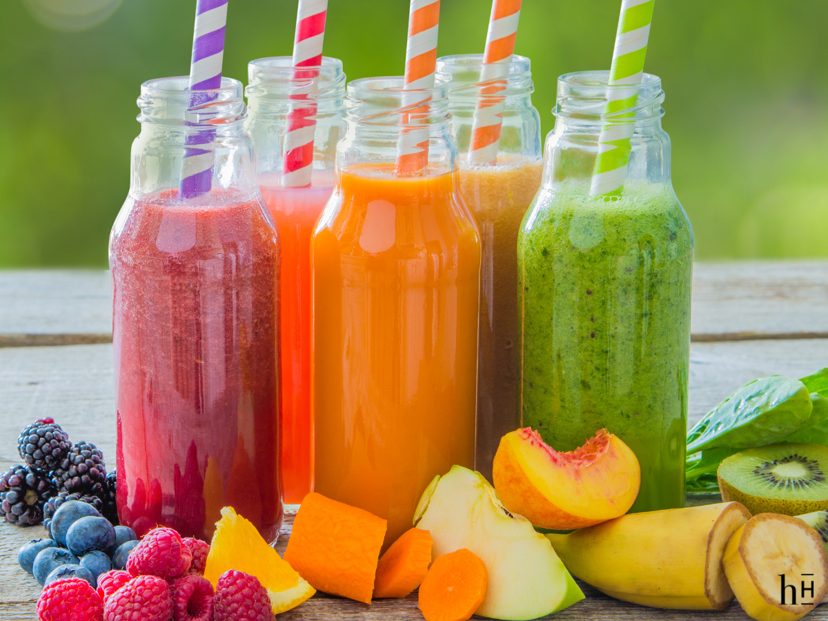 picture of 6oz plastic bottles filled with different flavors of smoothie and a straw near some fresh frui t