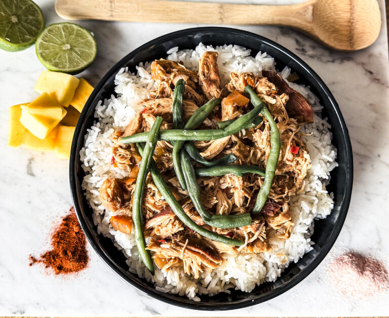 Slow cooker jerk mango chicken with tender shredded chicken in a rich, spicy-sweet jerk sauce topped with fresh mango chunks and lime served on top of white rice."