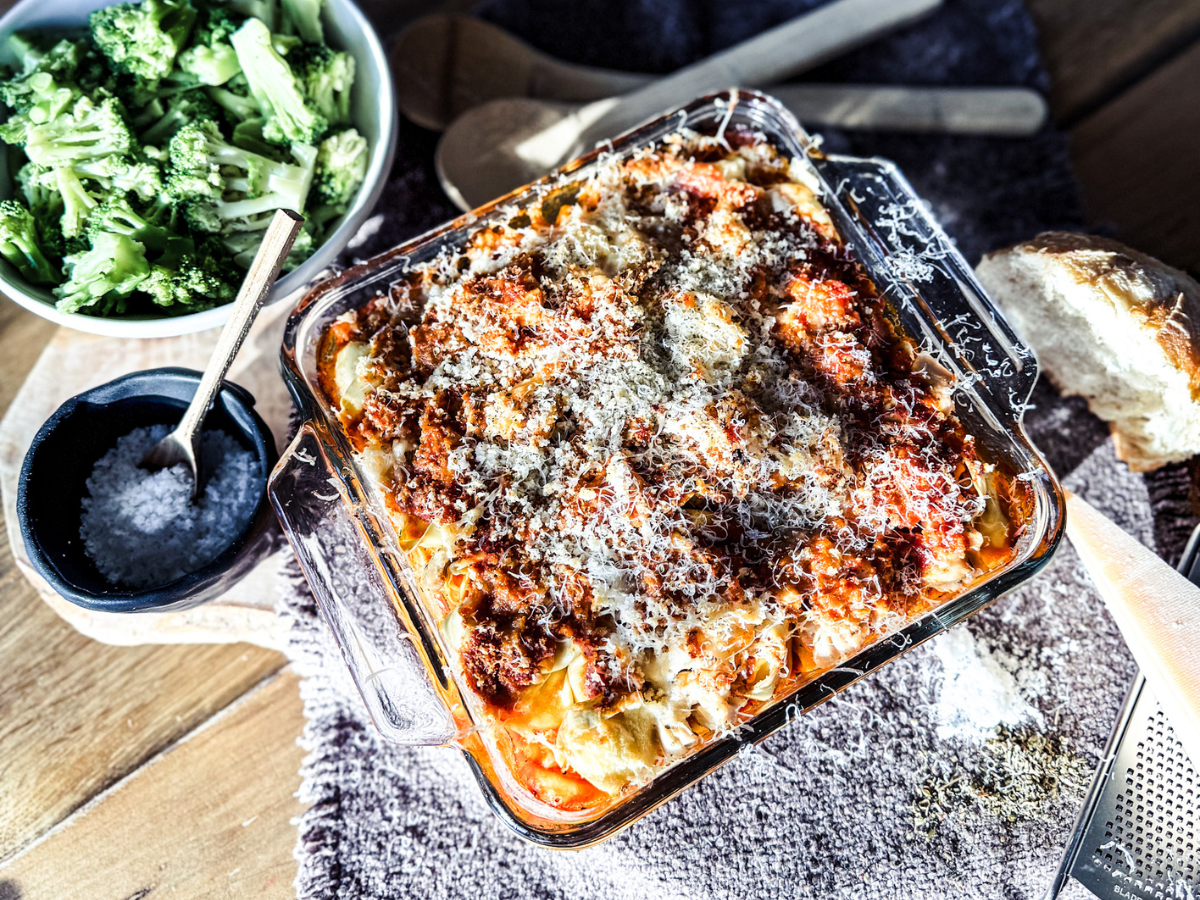 Square dish of chicken parmesan casserole with a small wooden bowl of salt and broccoli.