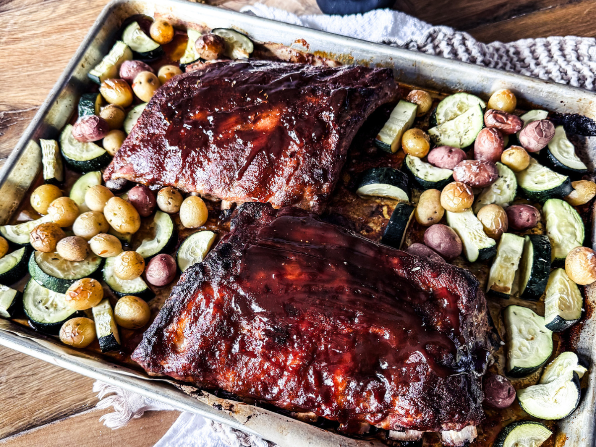 Ribs on a sheet pan seasoned surrounded by vegetables.
