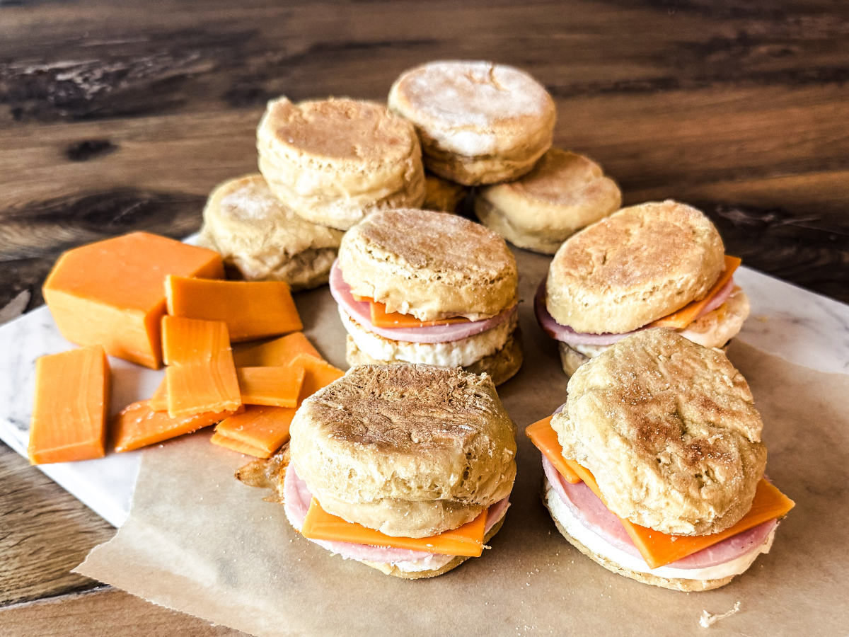 English Muffin Breakfast Sandwiches placed on parchment paper with a stack of cheese on the side.