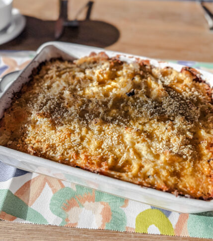 Cheesy potatoes in a white dis. Placed on a floral and wood backdrop.
