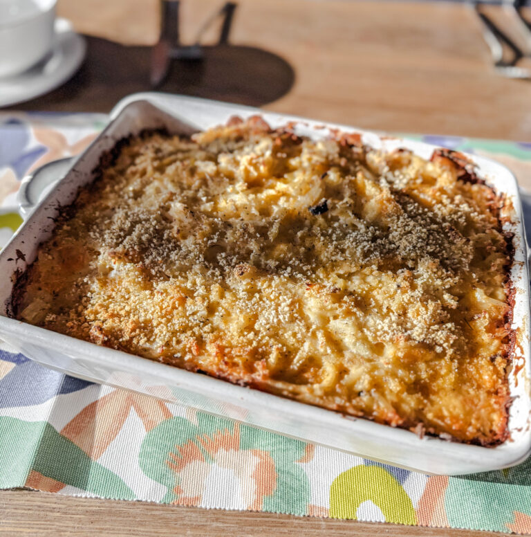 Cheesy potatoes in a white dis. Placed on a floral and wood backdrop.