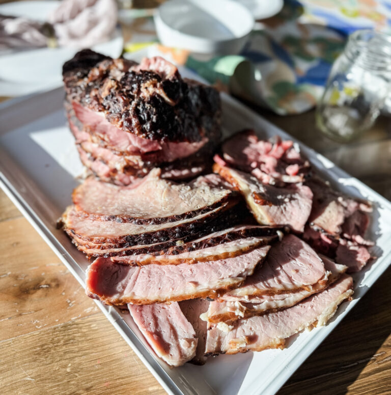 A spiral ham carved on a white platter placed on a wooden backdrop.