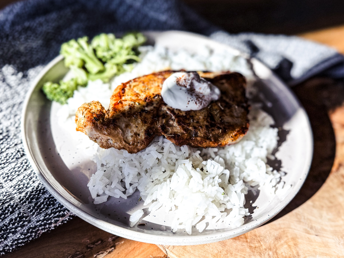 Chipotle Chicken on a bed of rice with broccoli on the side. A wooden back drop with a textured black and white towel underneath the plate.