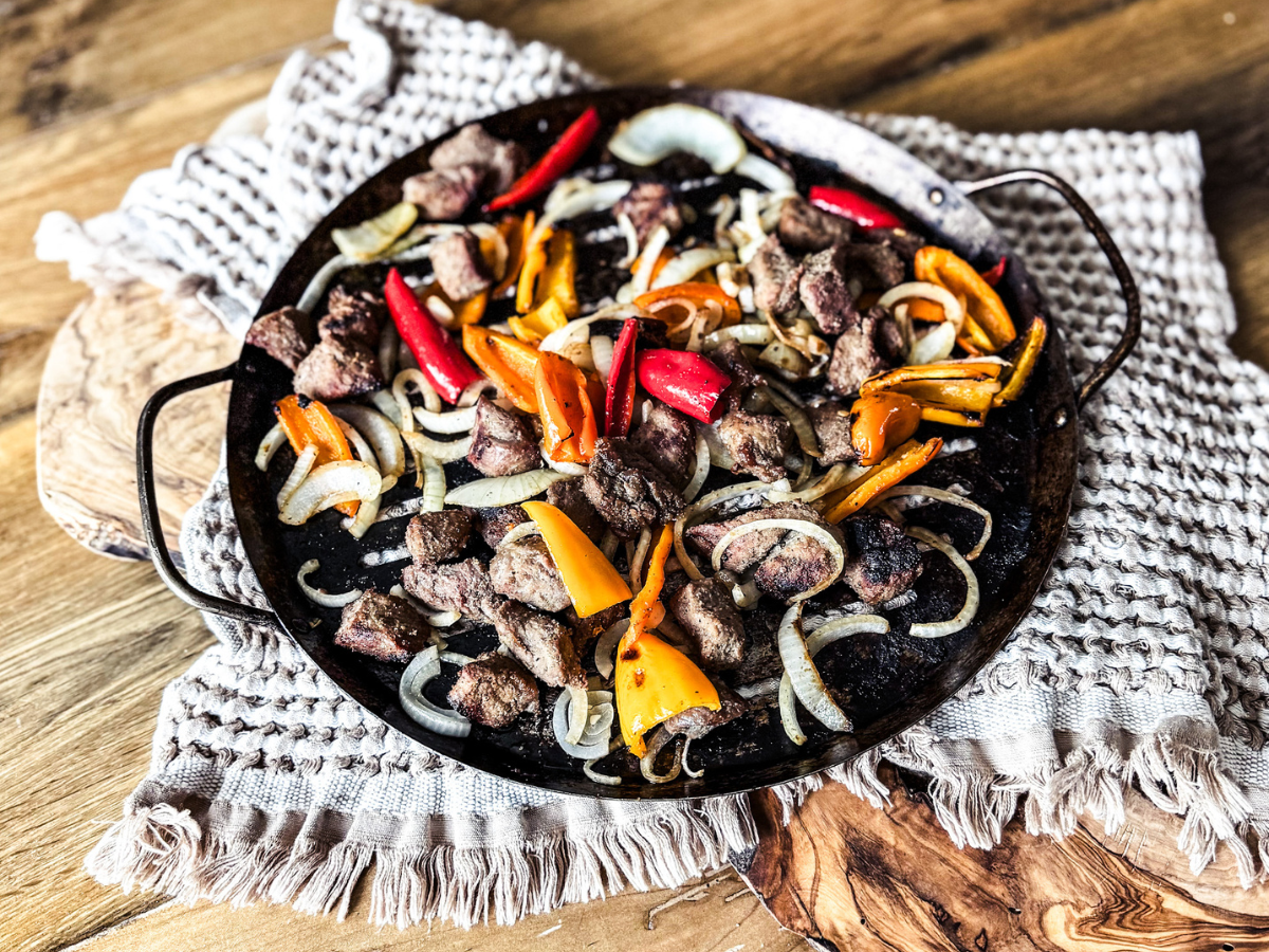 Deconstructed Steak Kebabs on a skillet with a tan background