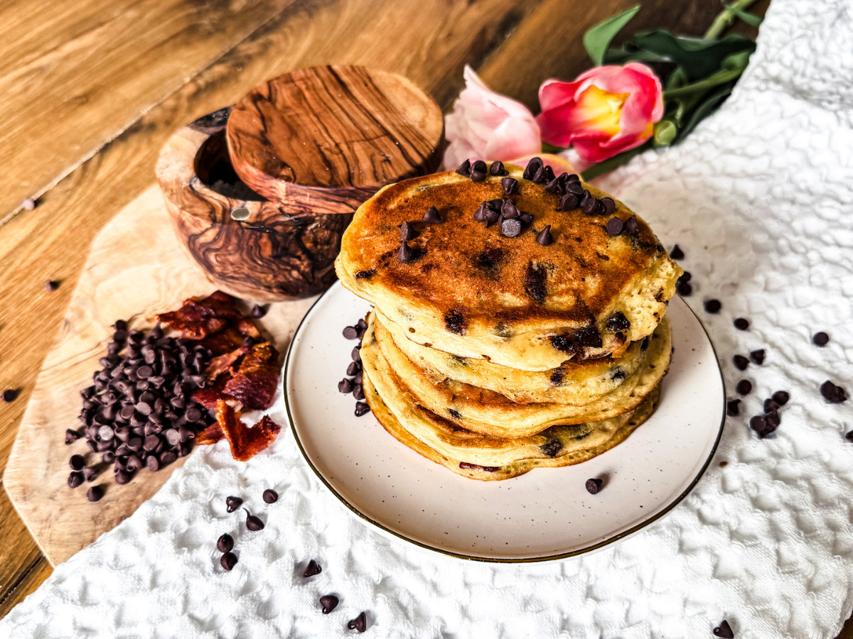 Bacon and Chocolate Chip Pancakes stacked on a small plate. to the left is a pile of Chocolate Chips with a little bowl for salt.