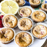 mini lemon and raspberry muffins on a circular white plate with lemons and raspberries on top.