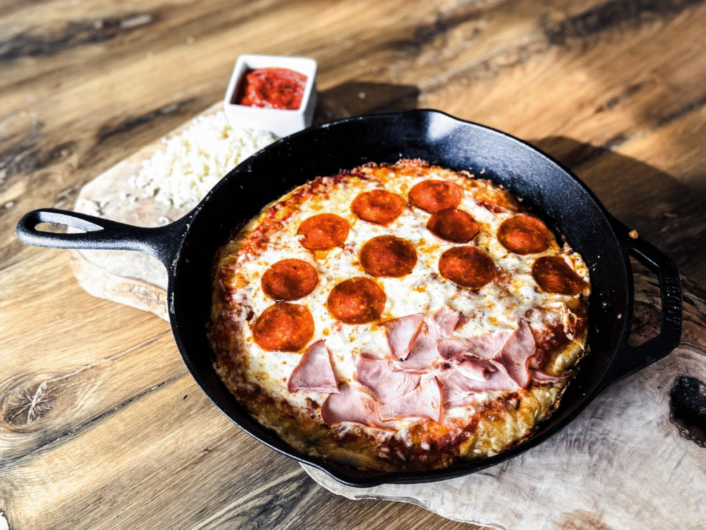 Pizza in a cast iron grill on a wooden background wit half pepperoni and half ham on top.