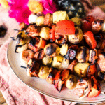 Pork Skewers on a white platter with a wooden backdrop . Birght pink peonies in the background.