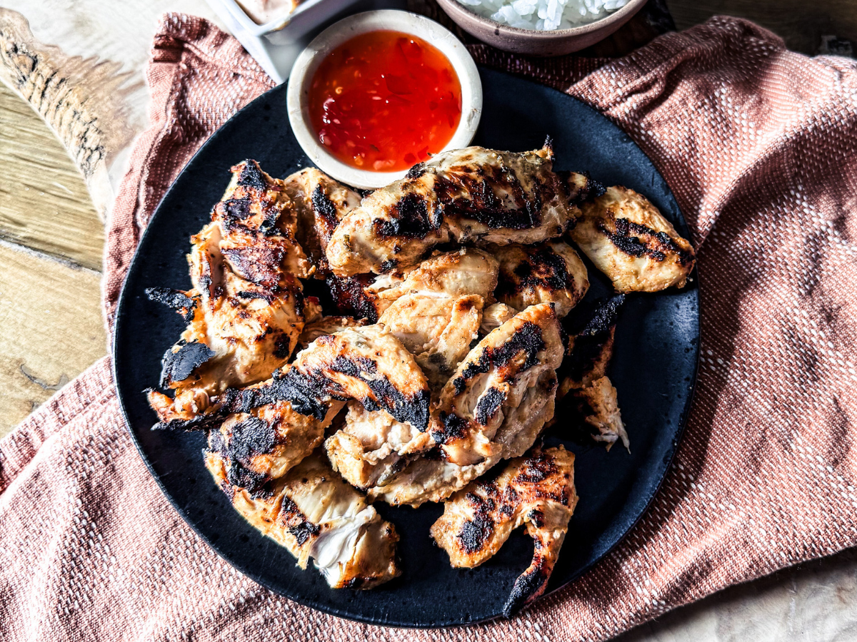 Bang Bang Chicken Piled on a black plate with an orange back drop and sweet chili sauce on the top in a small white dish.