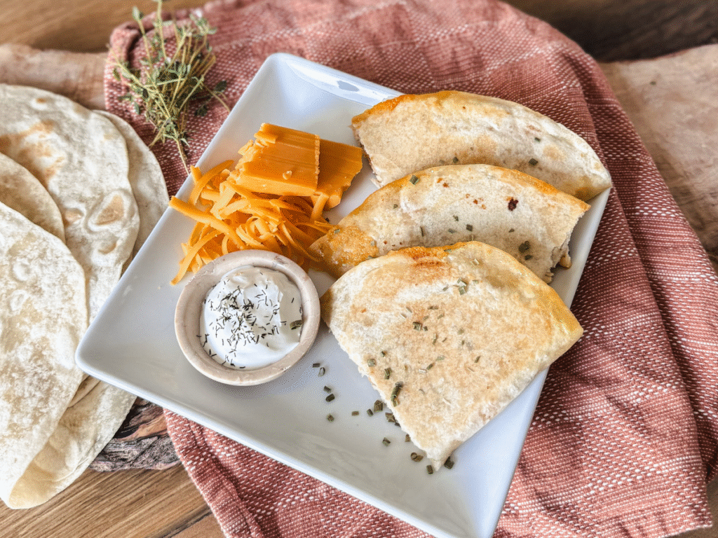 Ranch Chicken Quesadillas on a white platter with a side of sour cream and orange tea towel in the background
