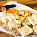 Sheet pan quesadillas on a wooden platter with cheese and zucchini in the background.
