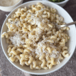 Cacio e pepe in a white bowl with gold spoon and brown backdrop.