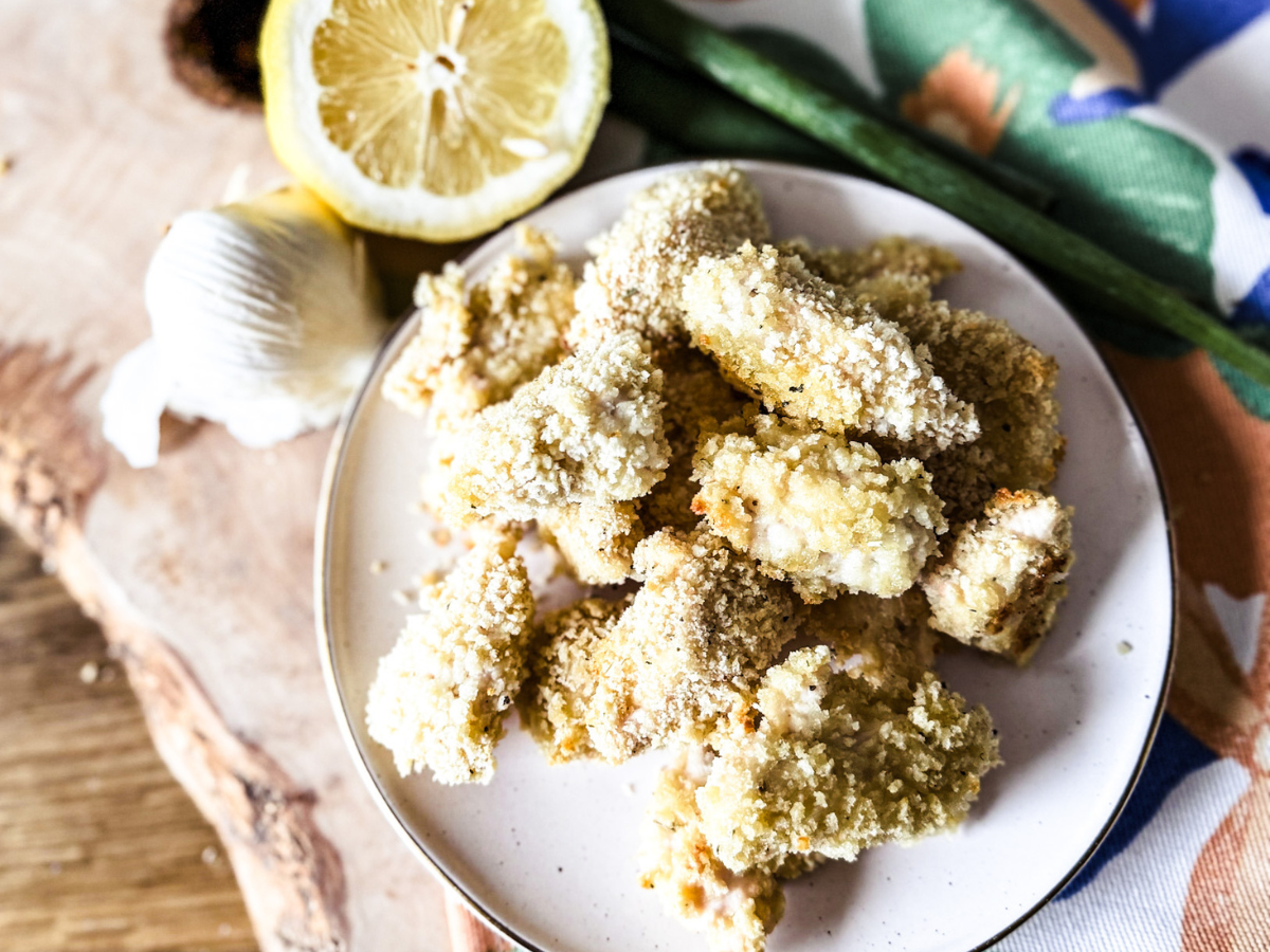 chicken bites piled on a white plate with lemon and garlic to the top left.