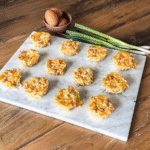 12 breakfast cups on a marble backdrop on a wood surface. Eggs and green onions to the top left.