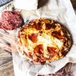 Mini pizza on parchment paper with a wooden backdrop.