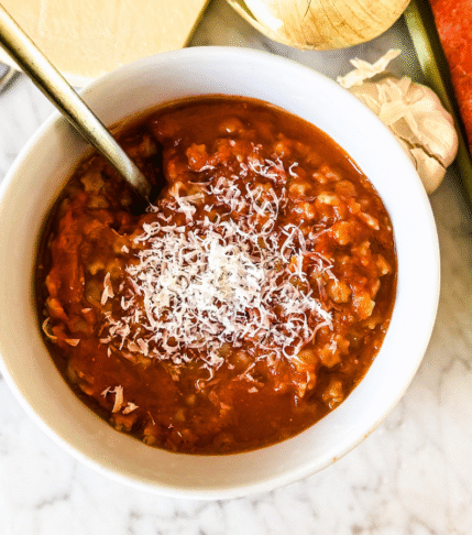 Homemade vegetable loaded spaghettios in a white bowl with gold spoon. Carrots, celery and onions on the upper right.
