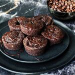 5 brownie bites stacked on a plate with chocolate chips in the background.