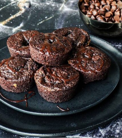5 brownie bites stacked on a plate with chocolate chips in the background.