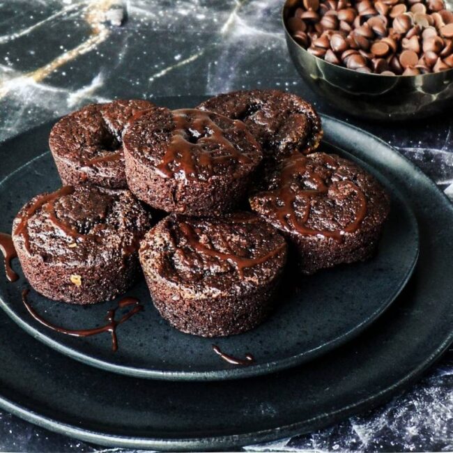 5 brownie bites stacked on a plate with chocolate chips in the background.