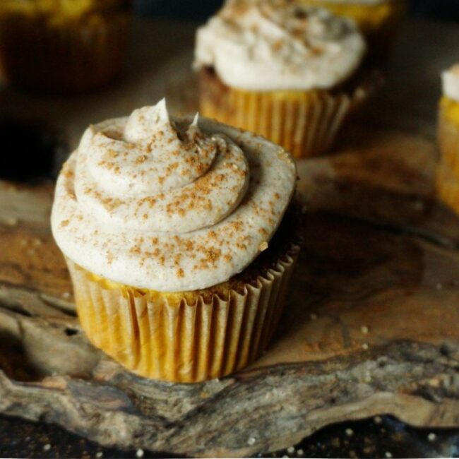 Pumpkin Cinnamon Roll muffin on a wooden board with a dark backdrop and cinnamon and sugar sprinkled on top.