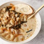 A bowl of No-Bean White Chicken Chili with a gold spoon to the top right and a slice of bread to the top left.