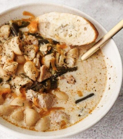 A bowl of No-Bean White Chicken Chili with a gold spoon to the top right and a slice of bread to the top left.