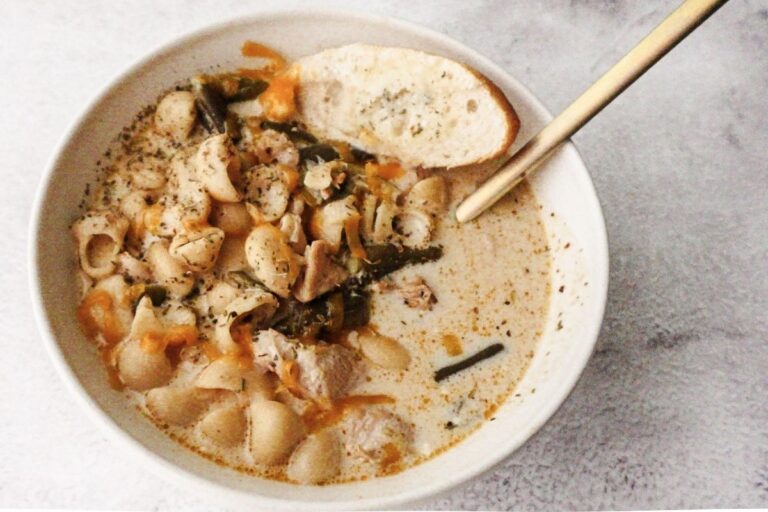 A bowl of No-Bean White Chicken Chili with a gold spoon to the top right and a slice of bread to the top left.