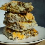 Square slices of sausage, potato and cheese stacked up.