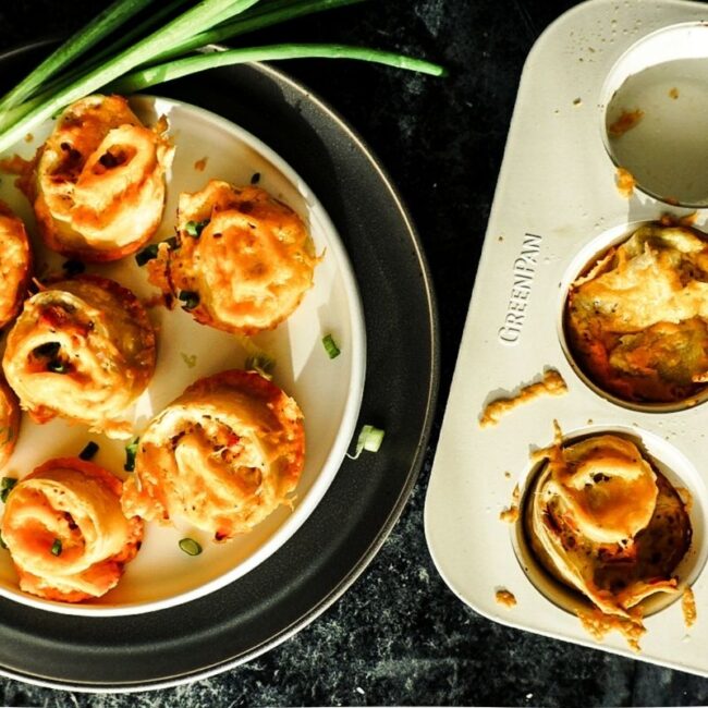 Boursin Tortilla Breakfast Rolls on a plate with a muffin tin to the right. Green onions sit to the top left.