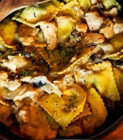 Chicken Stroganoff Ravioli in a skillet with a wooden spoon and thyme on top