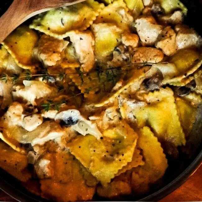 Chicken Stroganoff Ravioli in a skillet with a wooden spoon and thyme on top