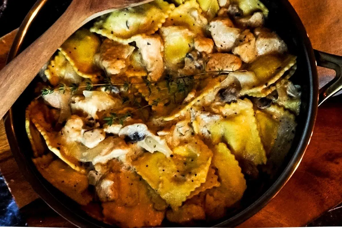 Chicken Stroganoff Ravioli in a skillet with a wooden spoon and thyme on top