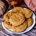 Pumpkin Snickeroodle Cookies stacked on a plate with a wooden backdrop. A