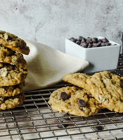 oatmeal chocolate chip cookies stacked on a wire rack. A pole of chocolate chips and oats are in the backdrop.