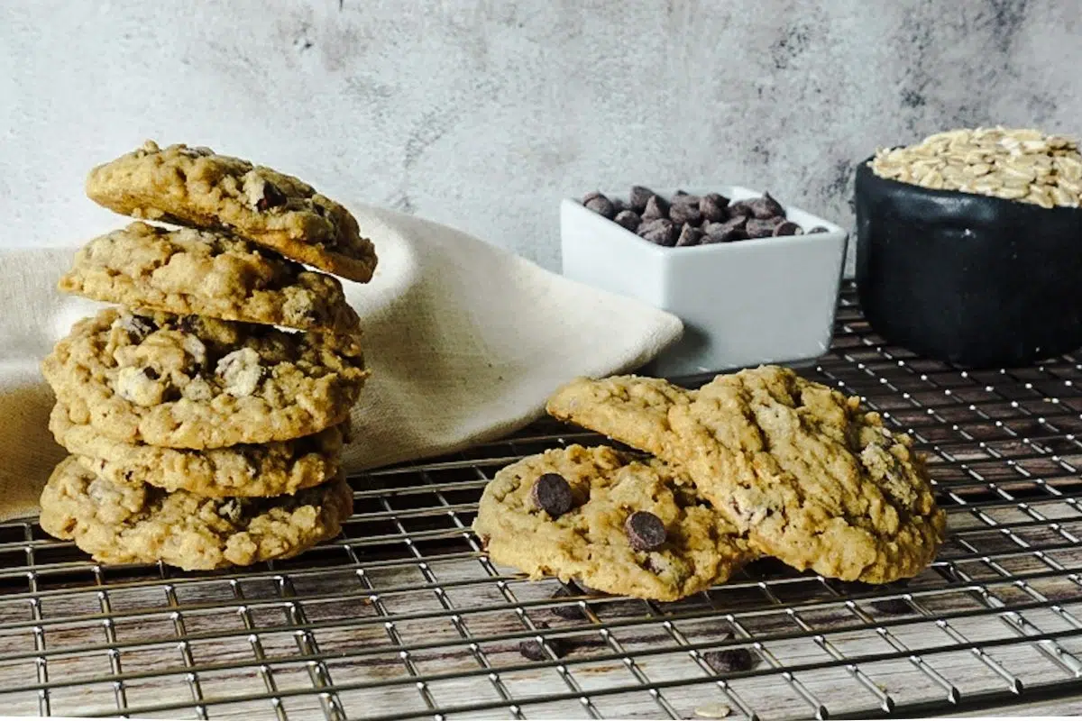 oatmeal chocolate chip cookies stacked on a wire rack. A pole of chocolate chips and oats are in the backdrop.